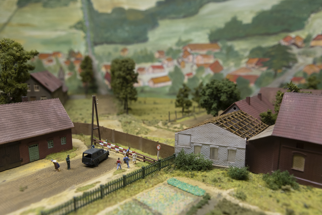 Modell eines Dorfes mit Häusern und einer Straße, die mit Grenzzäunen und einem Schlagbaum endet.