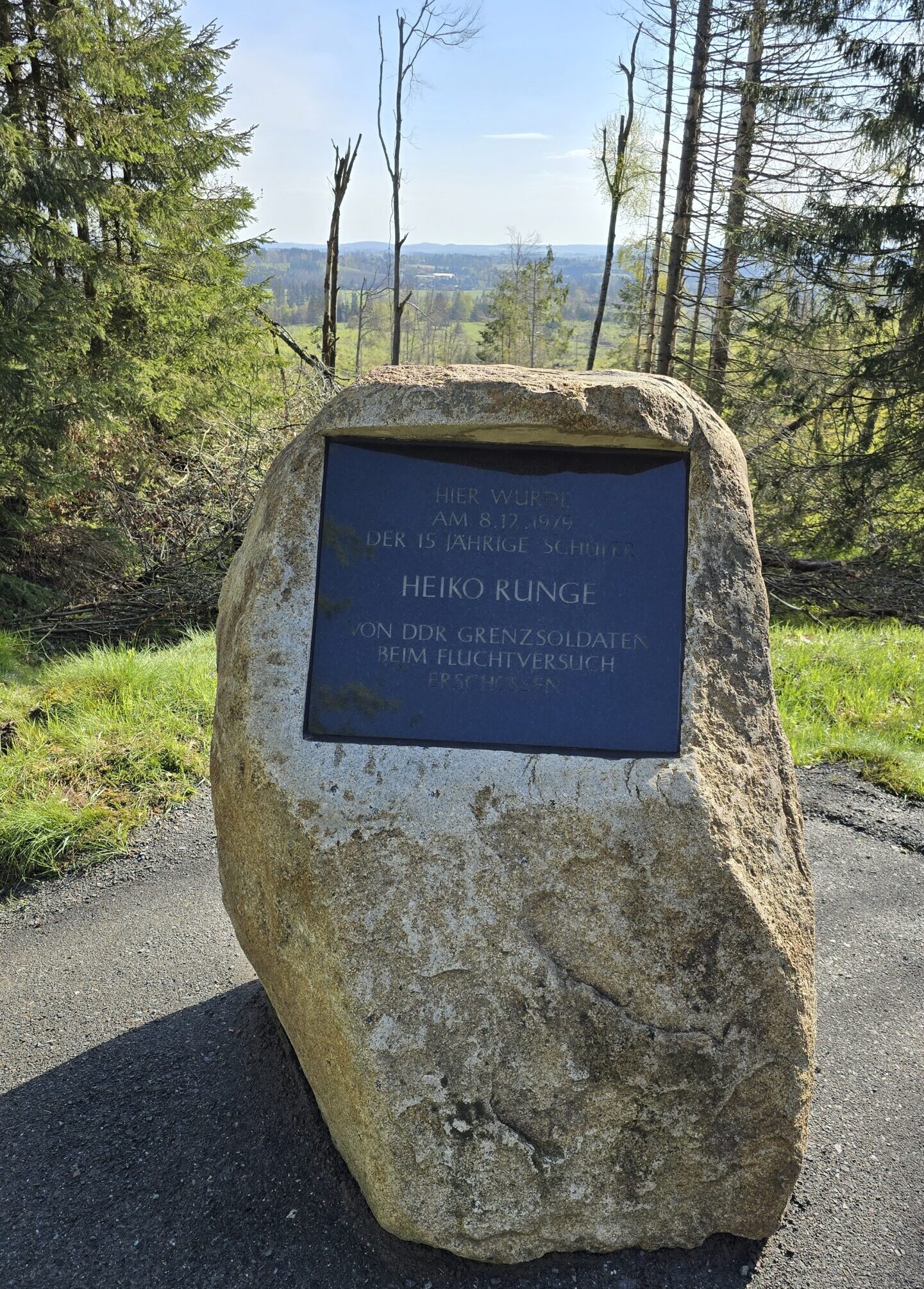 Frontale Ansicht des Gedenksteins für Heiko Runge. Im Hintergrund links und rechts Bäume. Direkt hinter dem Stein bietet sich ein weiter Blick über Felder und Wald.