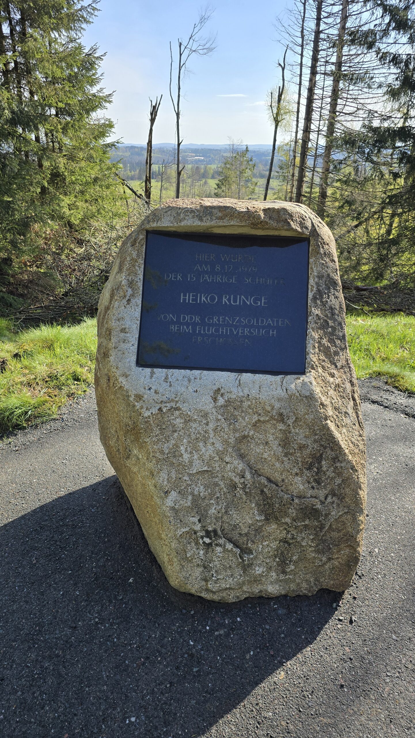Frontale Ansicht des Gedenksteins für Heiko Runge. Im Hintergrund links und rechts Bäume. Direkt hinter dem Stein bietet sich ein weiter Blick über Felder und Wald.