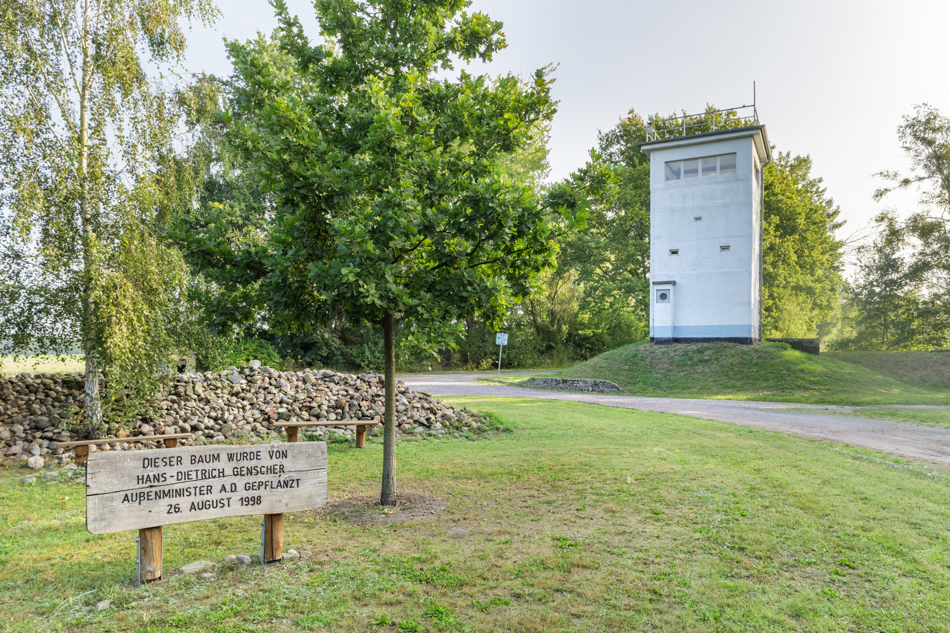 Ein heller Grenzturm steht etwas erhöht auf einer Grasfläche. Links ein Baum.